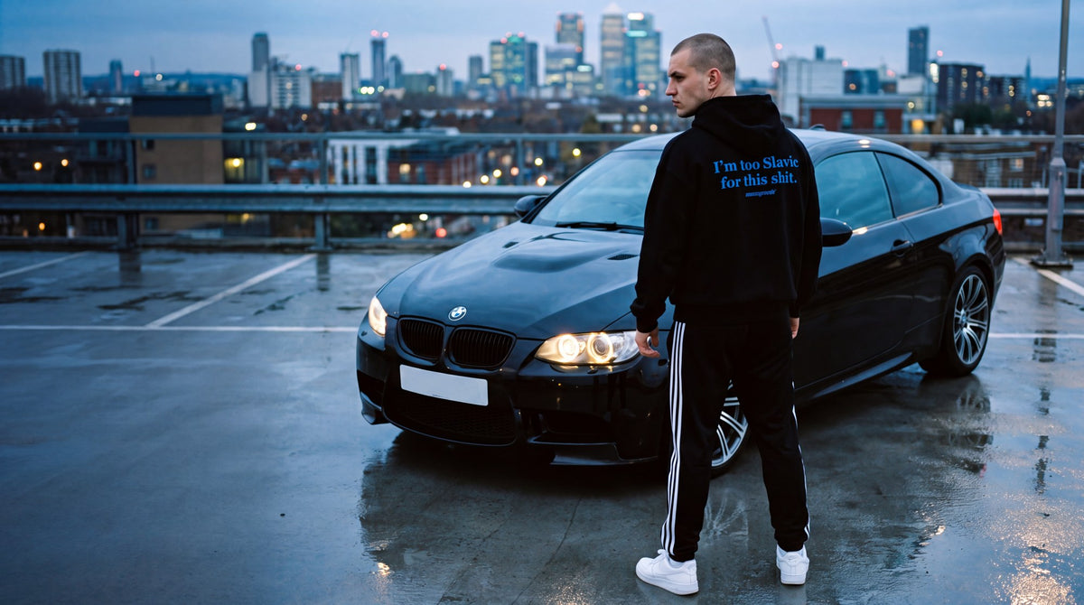 Man in a Common Grounds hoodie beside a black BMW coupe